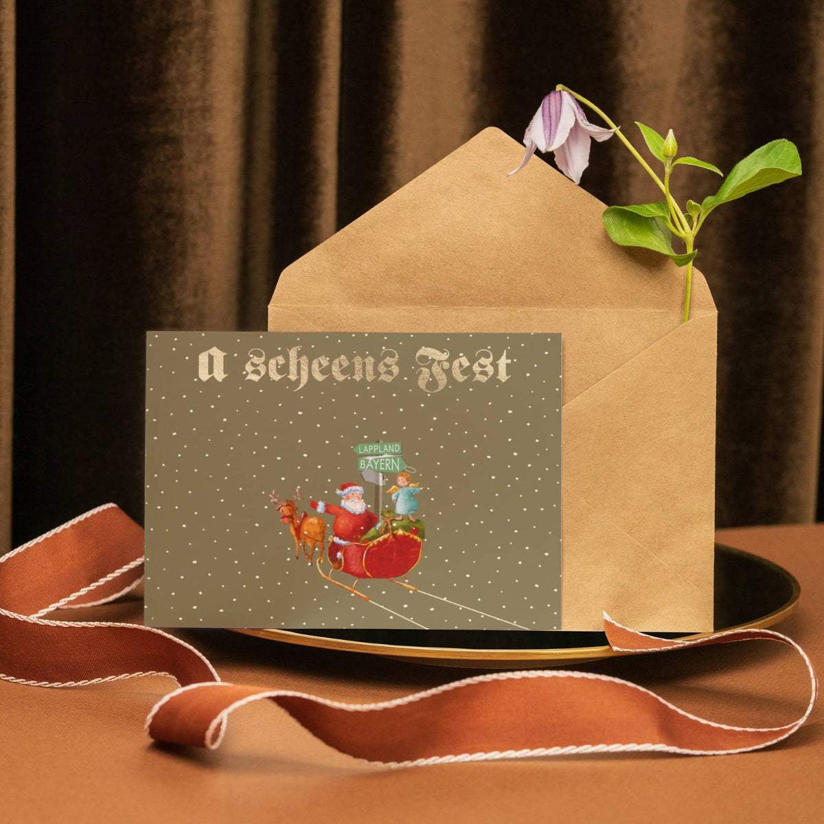 Glückwunschkarte "a scheens Fest" mit Nikolaus im roten Schlitten und Schneeflocken auf braunem Umschlag.