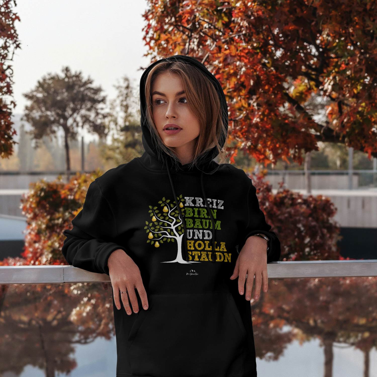Frau trägt schwarzen Hoodie Kreizbirnbaum mit Birnbaum-Motiv, Schriftzug und Kapuze in herbstlicher Umgebung.