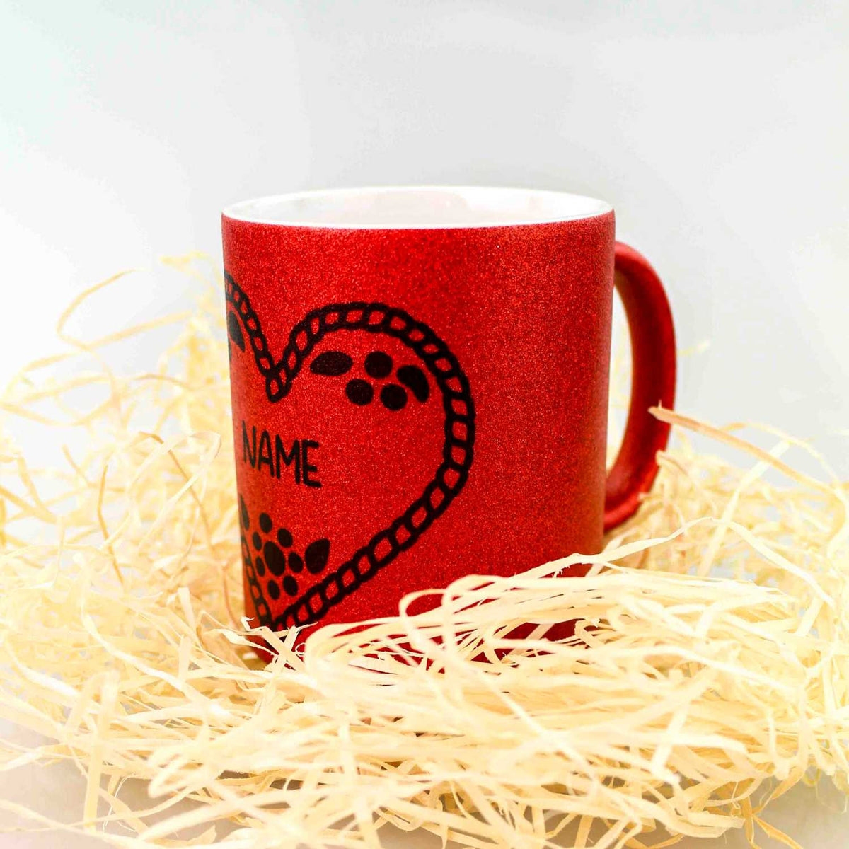 Glitzerndes rotes Kaffee Haferl Herzal mit filigranem schwarzem Herzmotiv und individuellem Namen in Holzwolle.