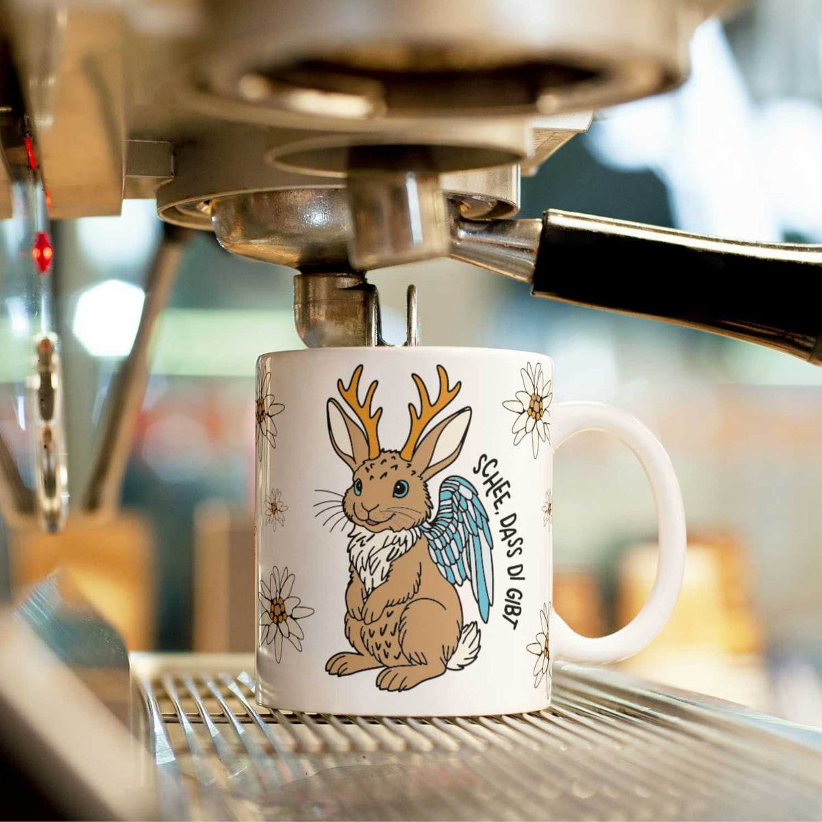 Kaffee Haferl Wolpertinger mit Hasenmotiv, Geweih, Flügeln und Edelweiß, unter Kaffeemaschine.