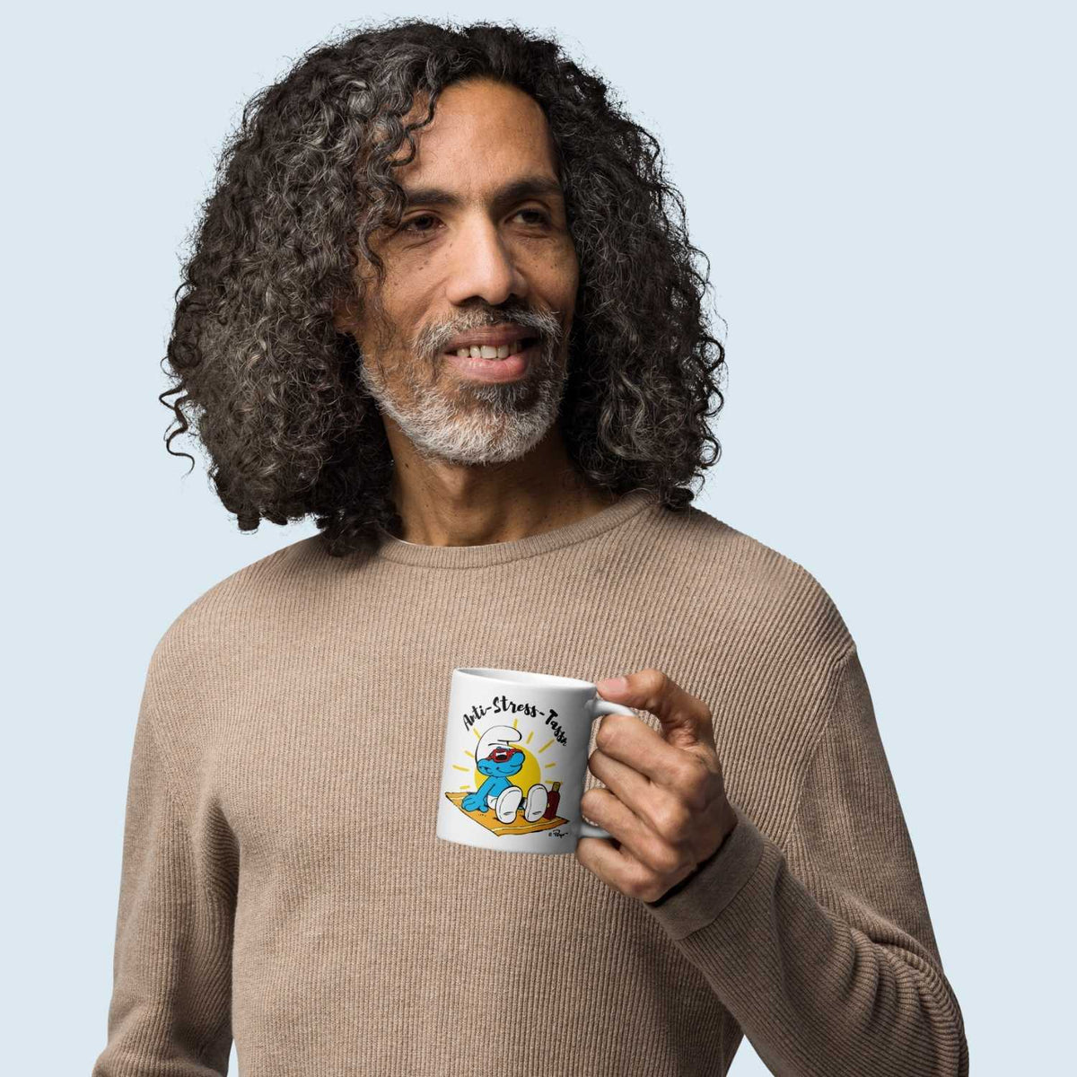 Mann mit grauen Locken hält eine weiße ®Die Schlümpfe Tasse Anti Stress Herren mit einem chillenden Schlumpf.