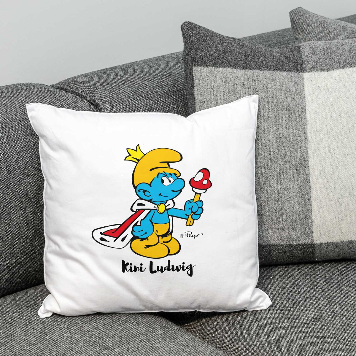 ®Die Schlümpfe Kini Kuschelkissen personalisiert mit Schlumpf im Königsoutfit und Pilz auf Sofa, gemütliches Geschenk