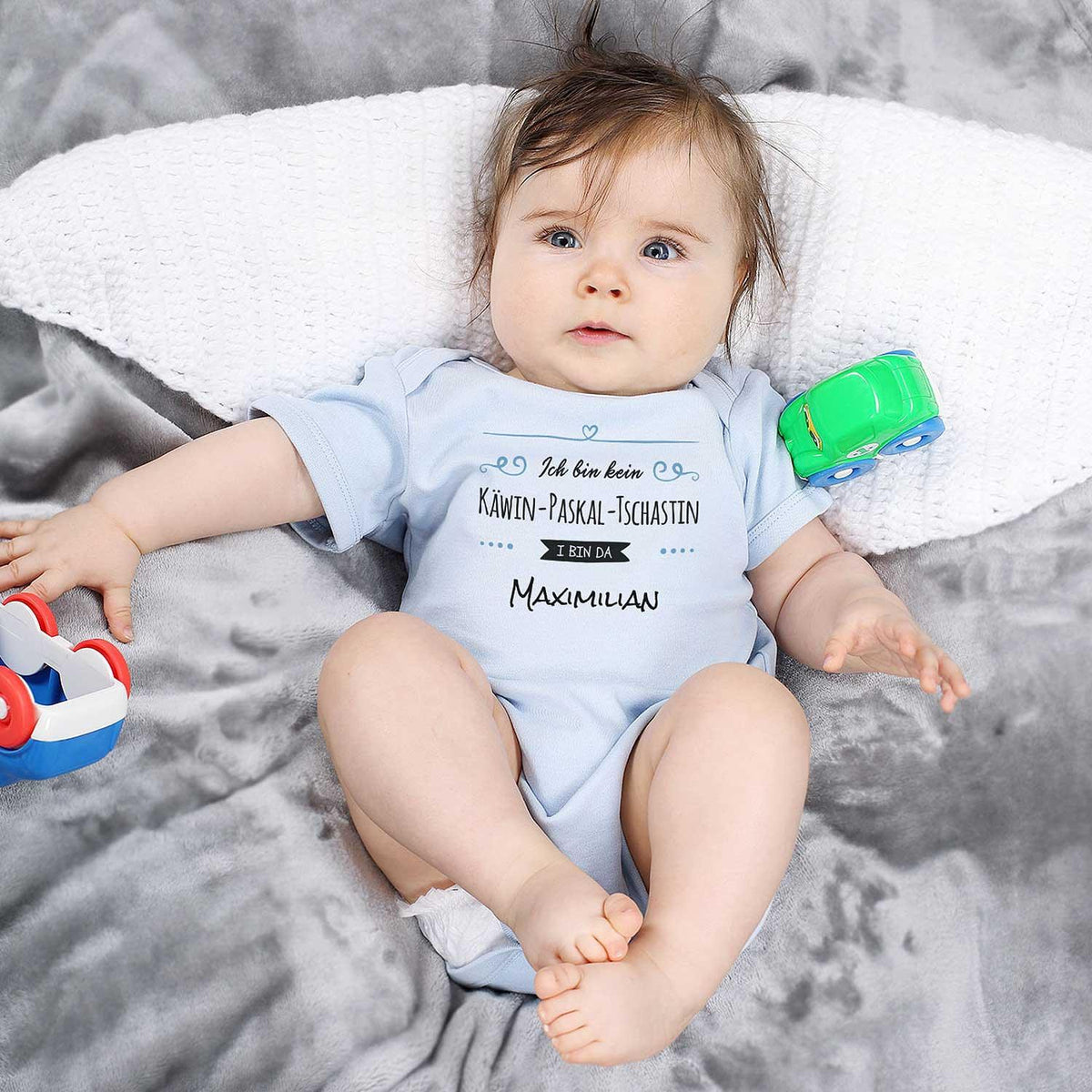Baby Body I bin da Wunschname in Hellblau mit personalisiertem Spruch auf weicher Decke.