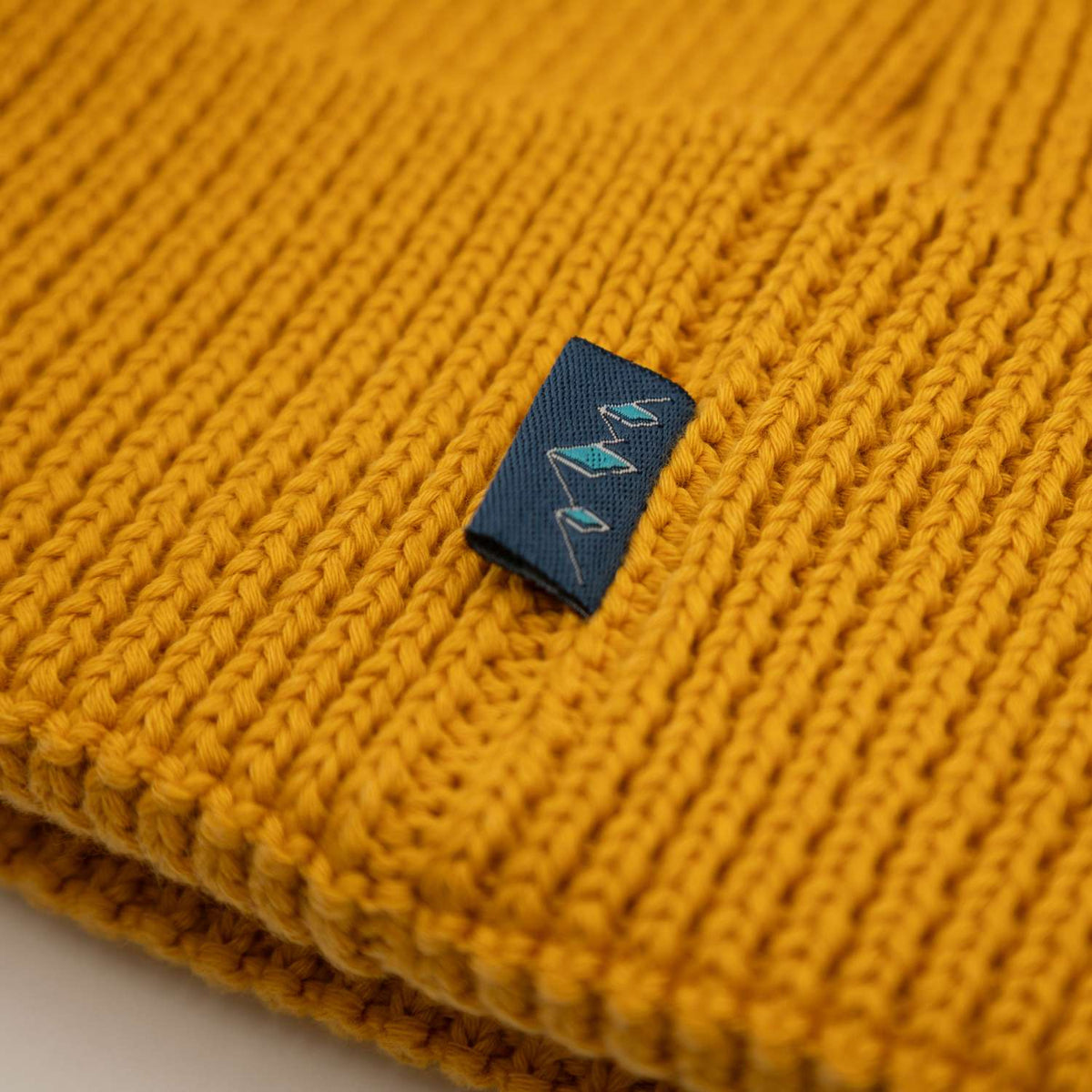 Ockergelbe Pumuckl Beanie aus Baumwolle, Rippstrick-Struktur und gewebtes Pumuckl-Label in der Gesamtansicht