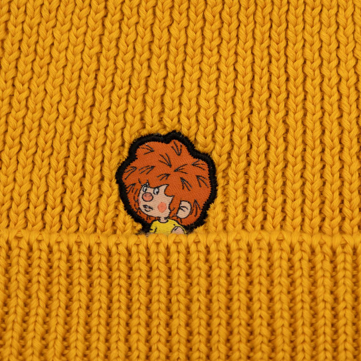 Nahaufnahme der ockergelben Pumuckl Beanie aus Baumwolle mit gewebtem Pumuckl-Label auf dem Umschlag