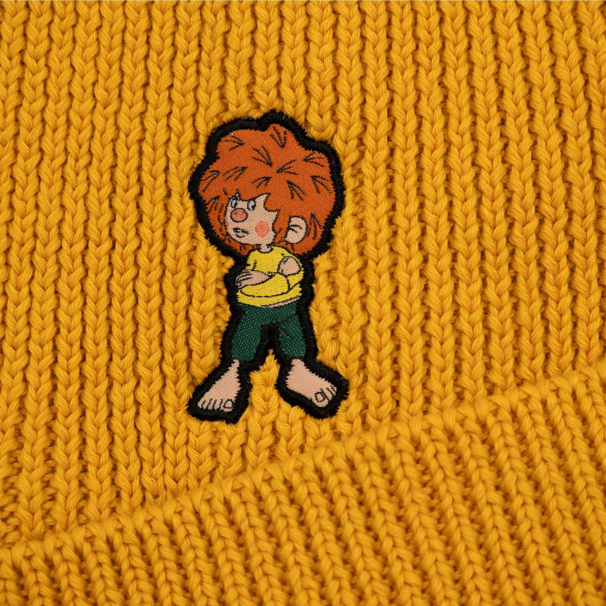 Detailansicht der ockergelben Pumuckl Beanie aus Baumwoll-Rippstrick mit gewebtem Pumuckl-Label