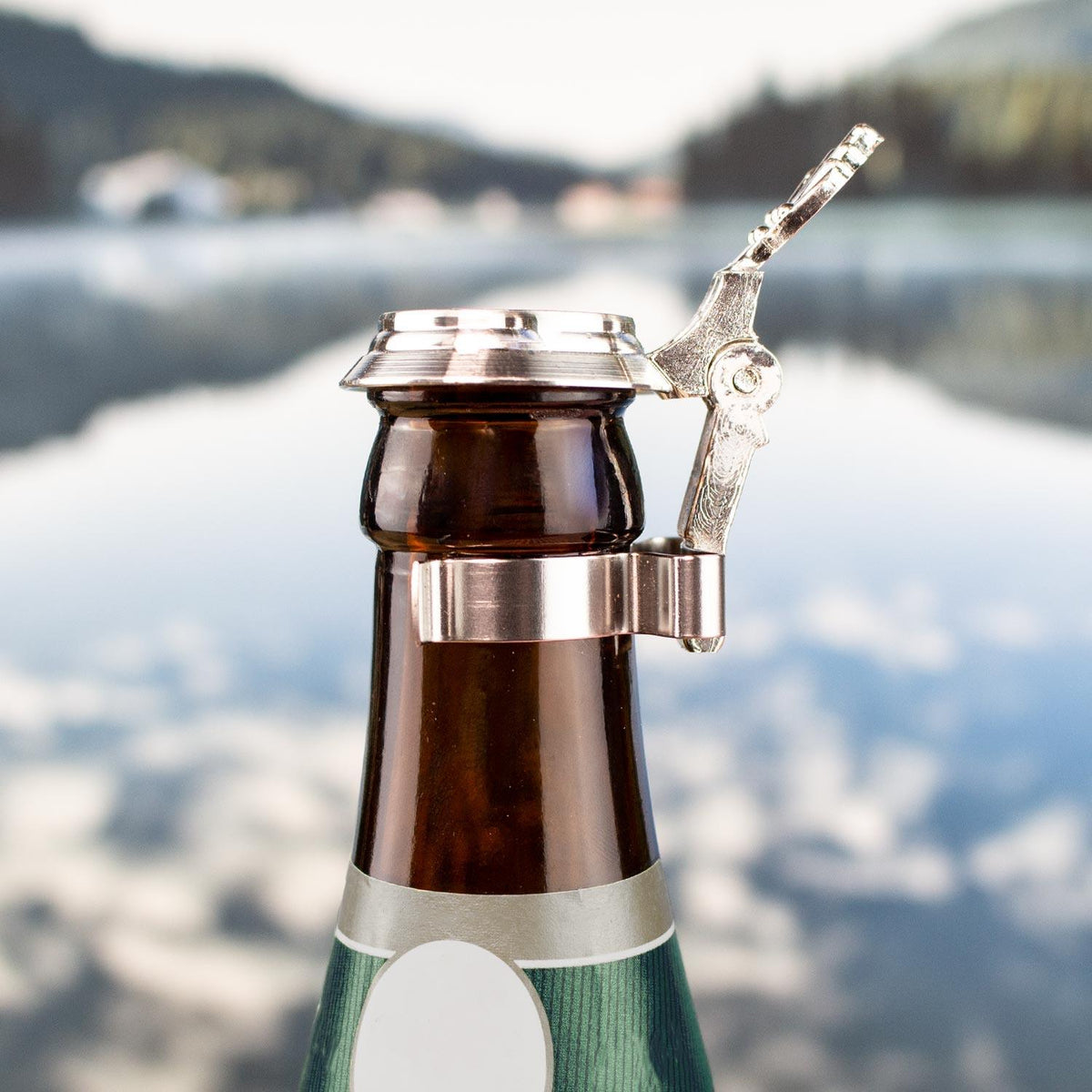 Bierflaschen Zinndeckel zum Aufstecken Bayern auf einer Bierflasche vor verschwommener Seenlandschaft.