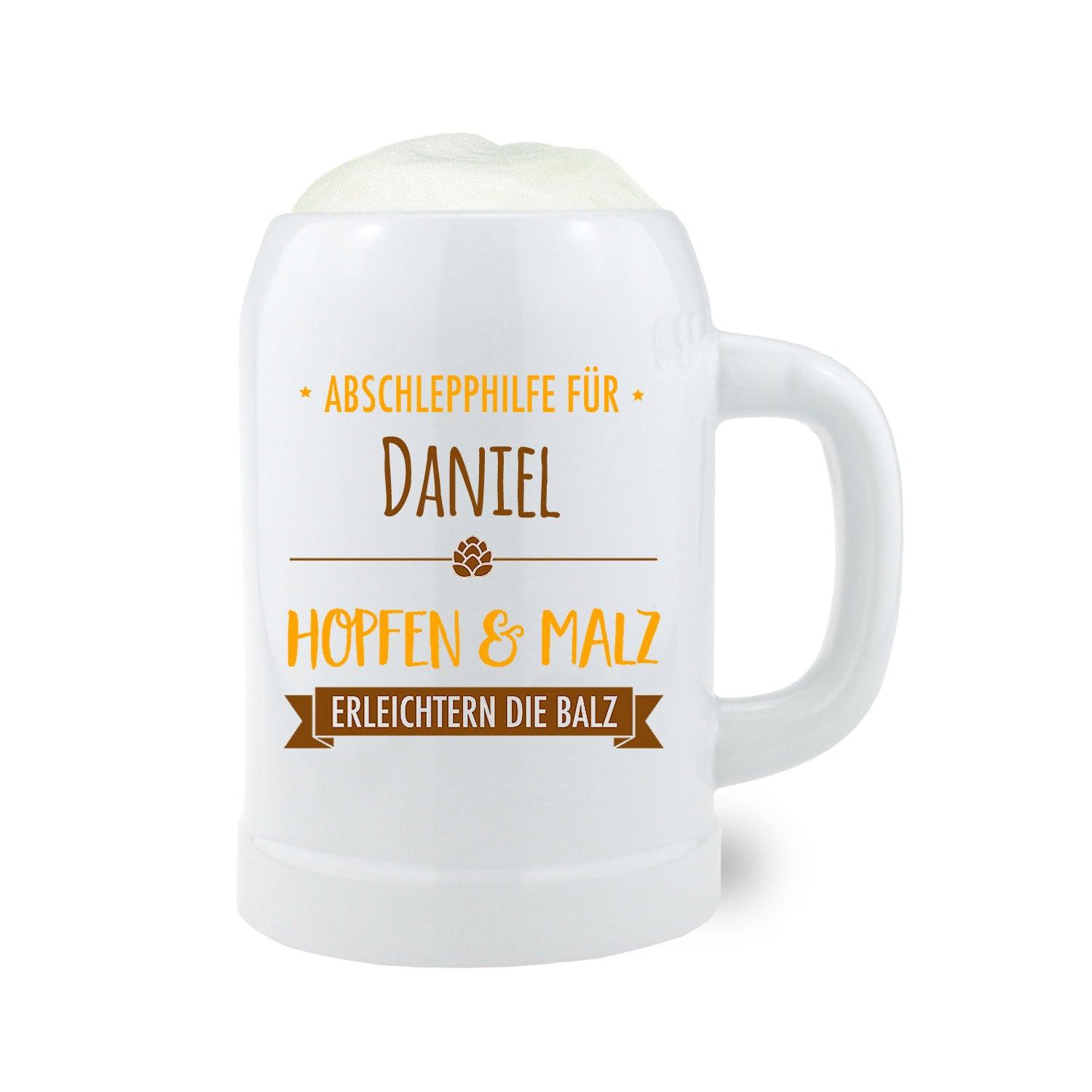 Weißer Bierkrug mit personalisiertem Spruch “Abschlepphilfe für Daniel – Hopfen & Malz erleichtern die Balz” und Schaumkrone.