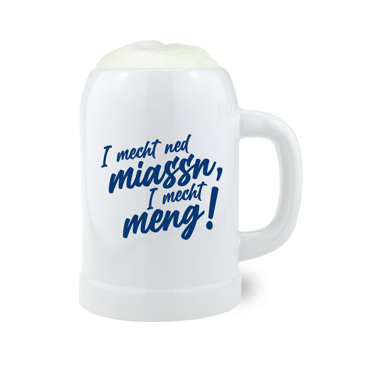 Weißer Bierkrug mit Aufschrift I mecht ned miassn, I mecht meng aus Keramik, gefüllt mit frischem Schaumbier.