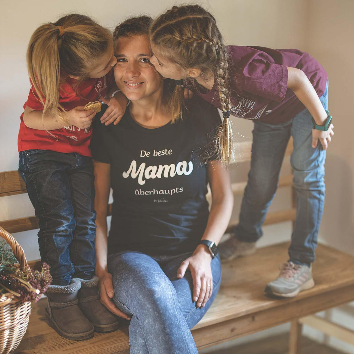Lachende Mama mit schwarzem Damen T-Shirt De beste Mama übahaupts, von zwei Kindern umarmt.