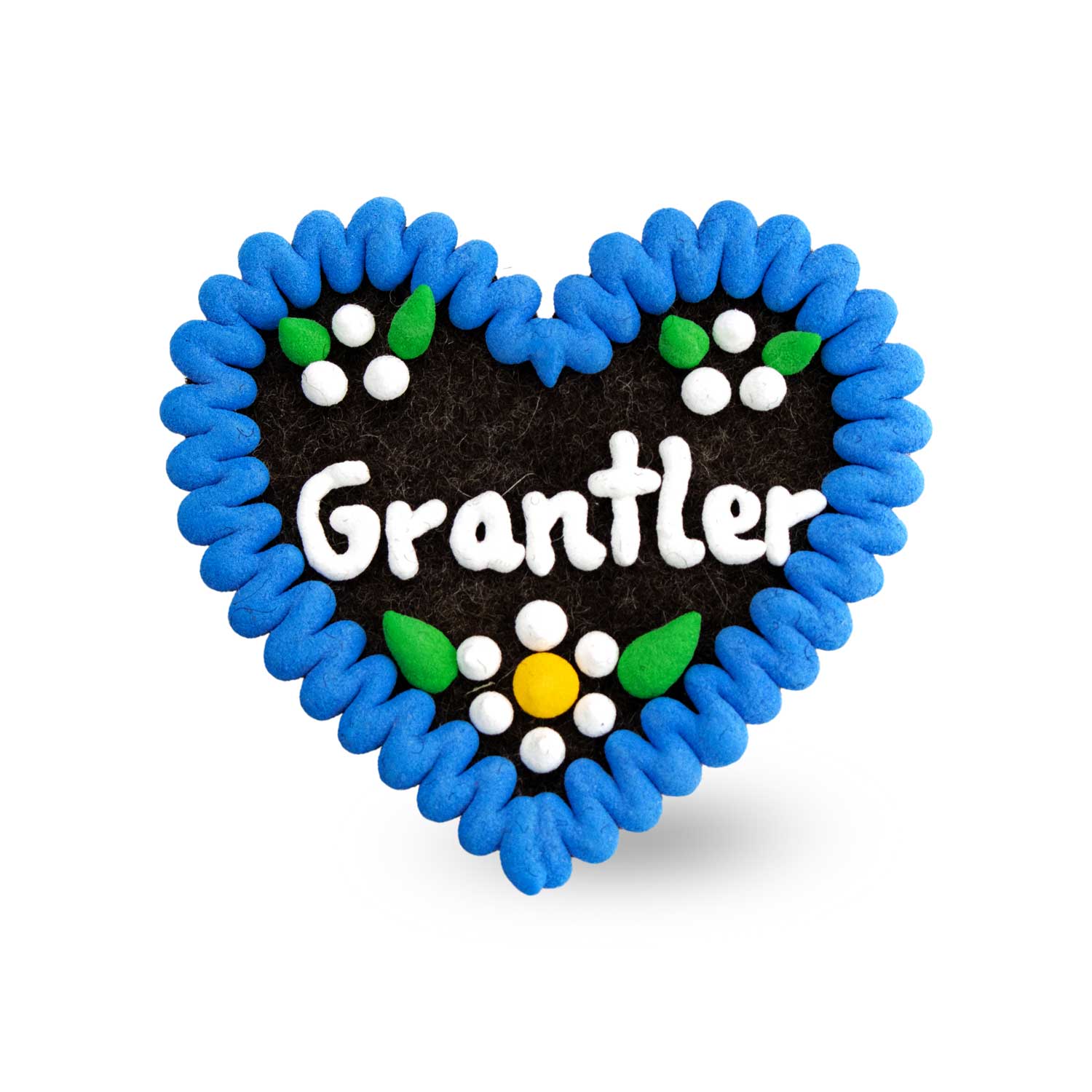 Blauer Filzherz-Anstecker Grantler mit weißer Aufschrift, grünen Blättern und weißen Blüten auf dunklem Hintergrund.
