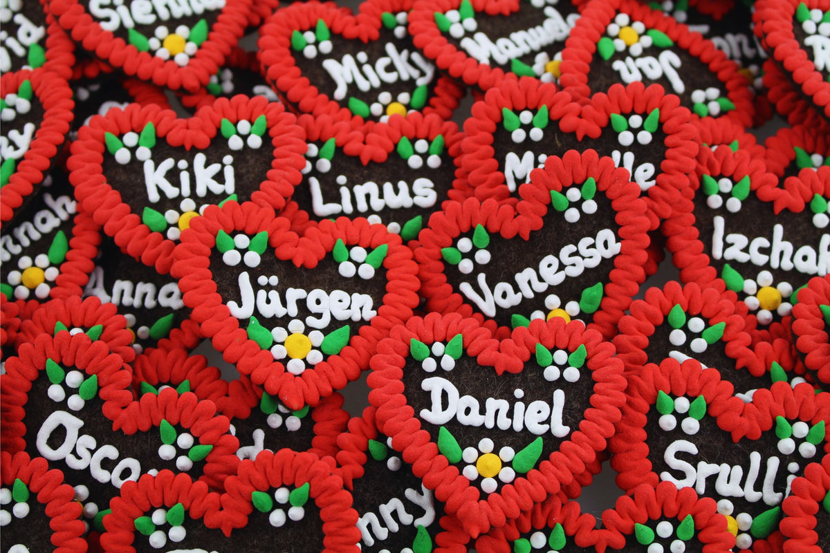 Personalisierte Lebkuchenherzen mit rotem Rand, bunten Zuckerblumen und Namen in weißer Schrift, beliebte Souvenirs.