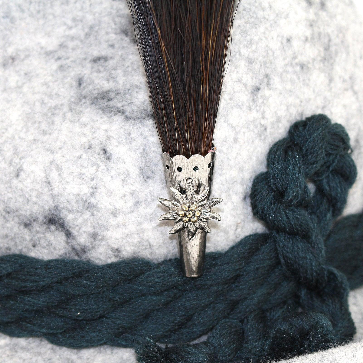 Traditioneller Trachtenhut aus grauem Filz mit Gamsbart und Edelweiß-Anstecker aus Silber, darunter ein dunkelgrünes Band.