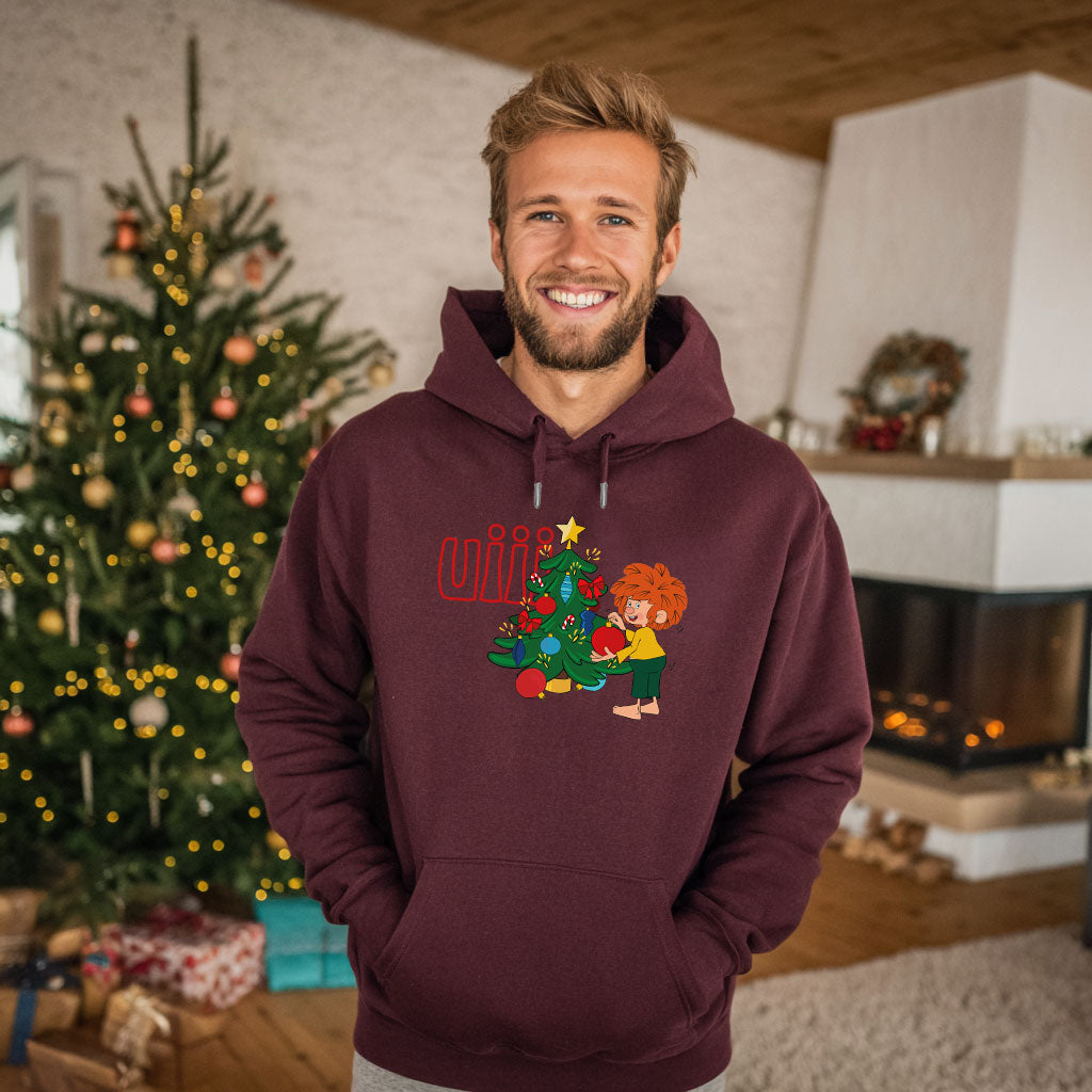 Mann im weinroten Pumuckl Hoodie Weihnachten vor geschmücktem Christbaum – Weihnachts-Hoodie für Herren