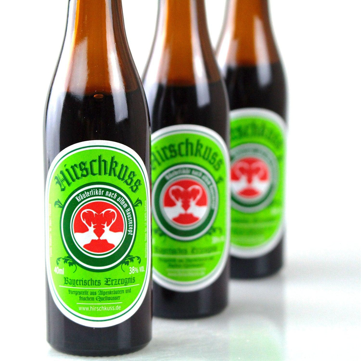 Drei braune Glasflaschen Hirschkuss Kräuterlikör 40ml mit grasgrünen Etiketten und Hirschköpfen.