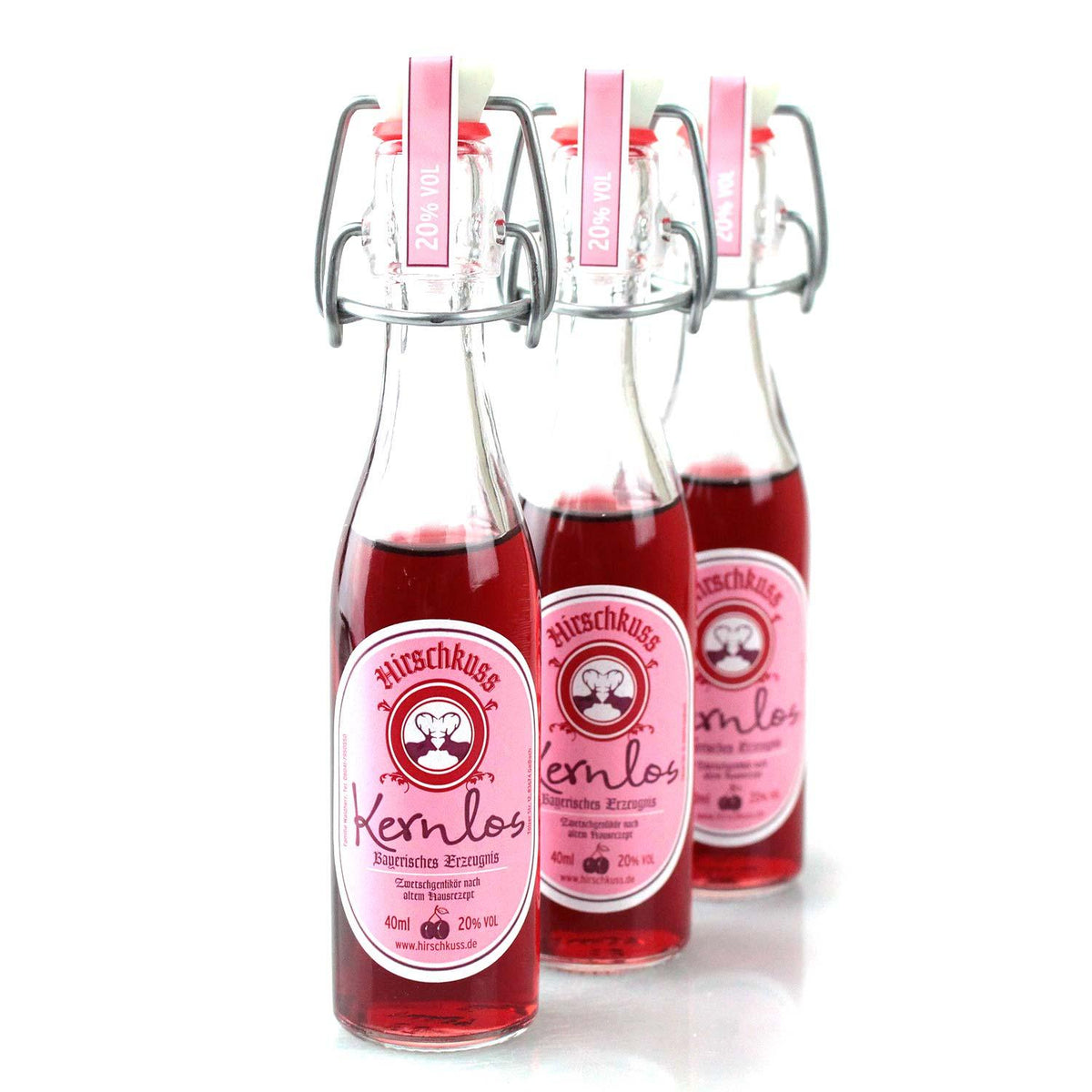 Drei Fläschchen Hirschkuss Kernlos Zwetschgenlikör in Reihe, mit Bügelverschluss und rosa Etikett.