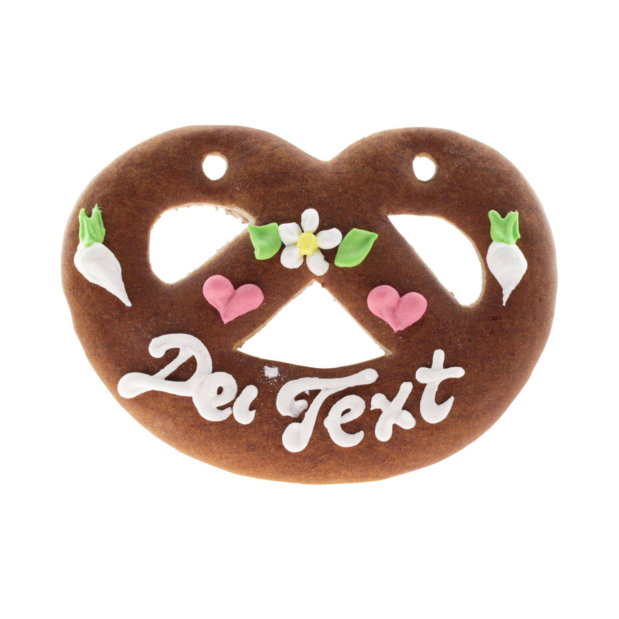 Lebkuchenherz Brezel mit weißer Aufschrift "Dei Text", rosa Herzen und zierenden Blumen und Radieschen.