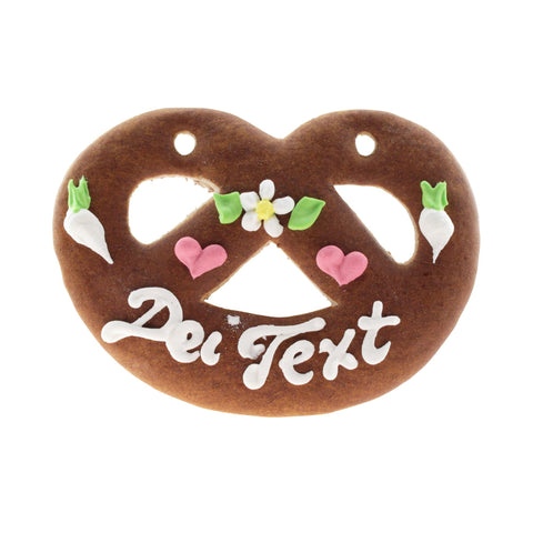 Lebkuchenherz Brezel mit weißer Aufschrift "Dei Text", rosa Herzen und zierenden Blumen und Radieschen.