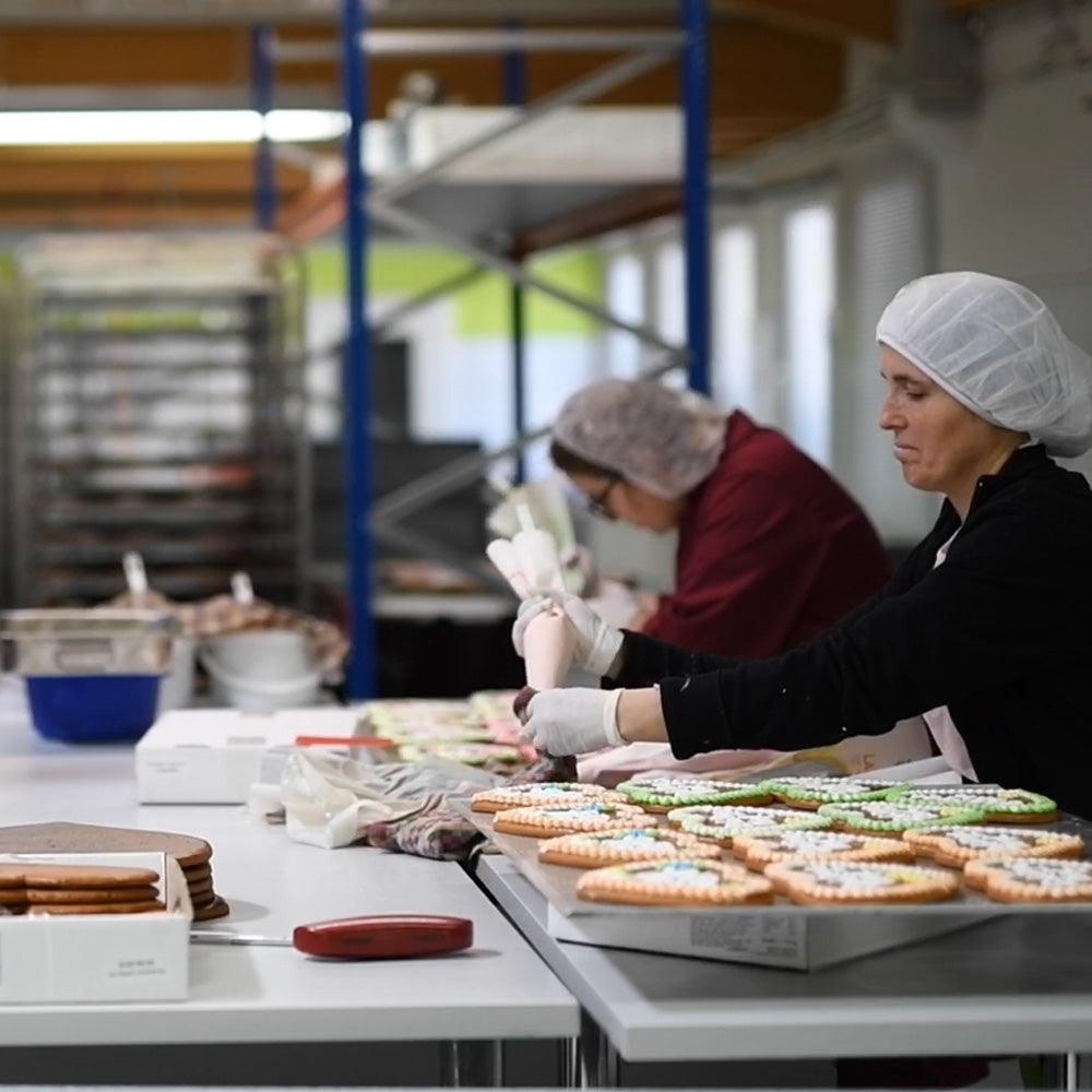 Mitarbeiterinnen dekorieren in einer Backstube sorgfältig Lebkuchen und Gebäck mit frischem Zuckerguss.