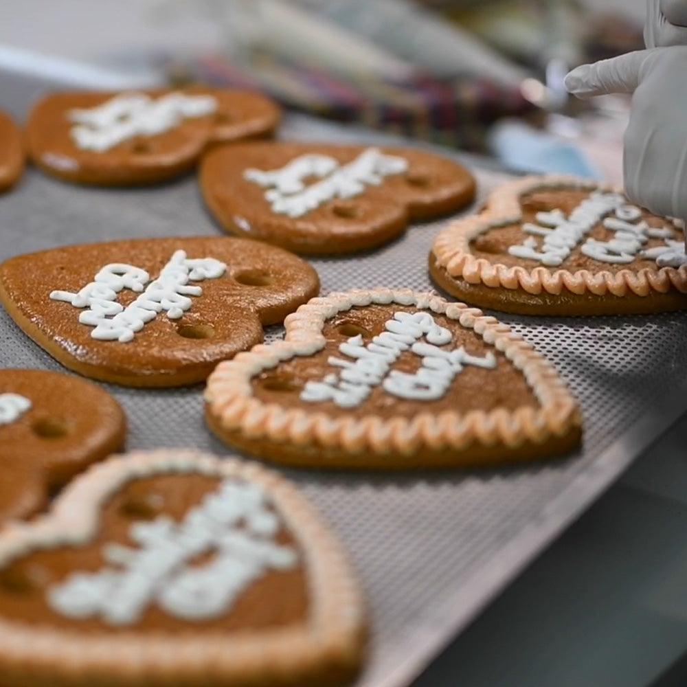 Herstellung von traditionellen Lebkuchenherzen mit Zuckerguss-Verzierung auf Backblechen in einer Bäckerei.