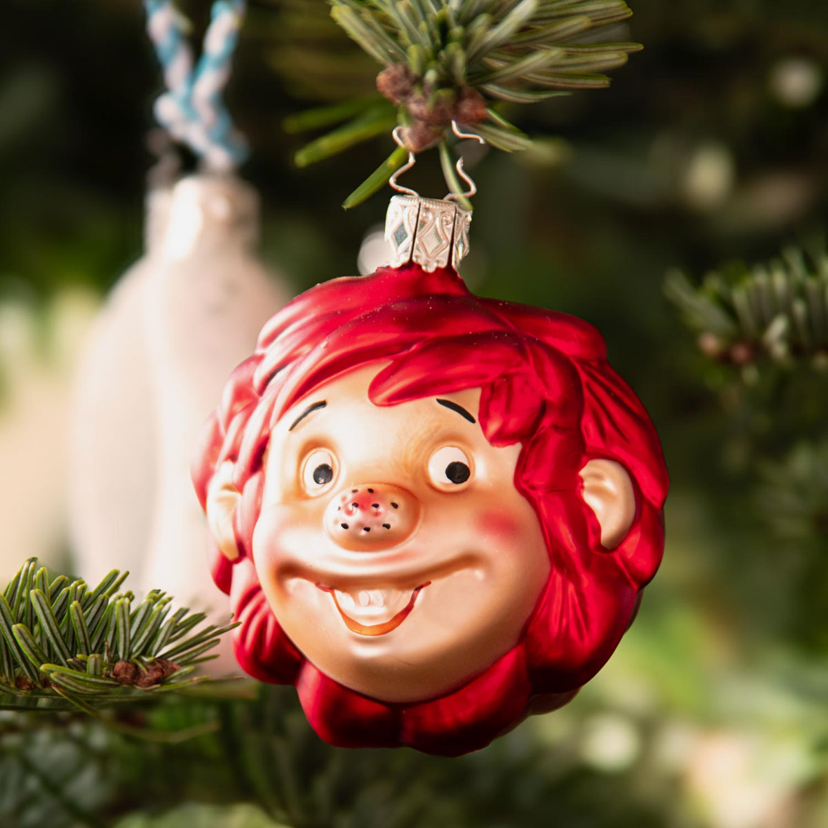 Pumuckl Weihnachtskugel aus Glas, detailreich mit rotem Haar, an einem Weihnachtsbaum hängend.