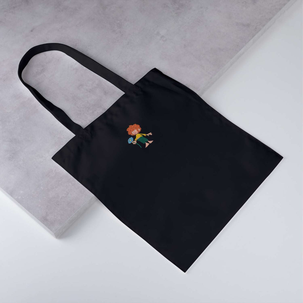 Schwarze Pumuckl Tasche "Schabernack" mit rothaarigem Kobold-Motiv, der blaue Blumen hält.