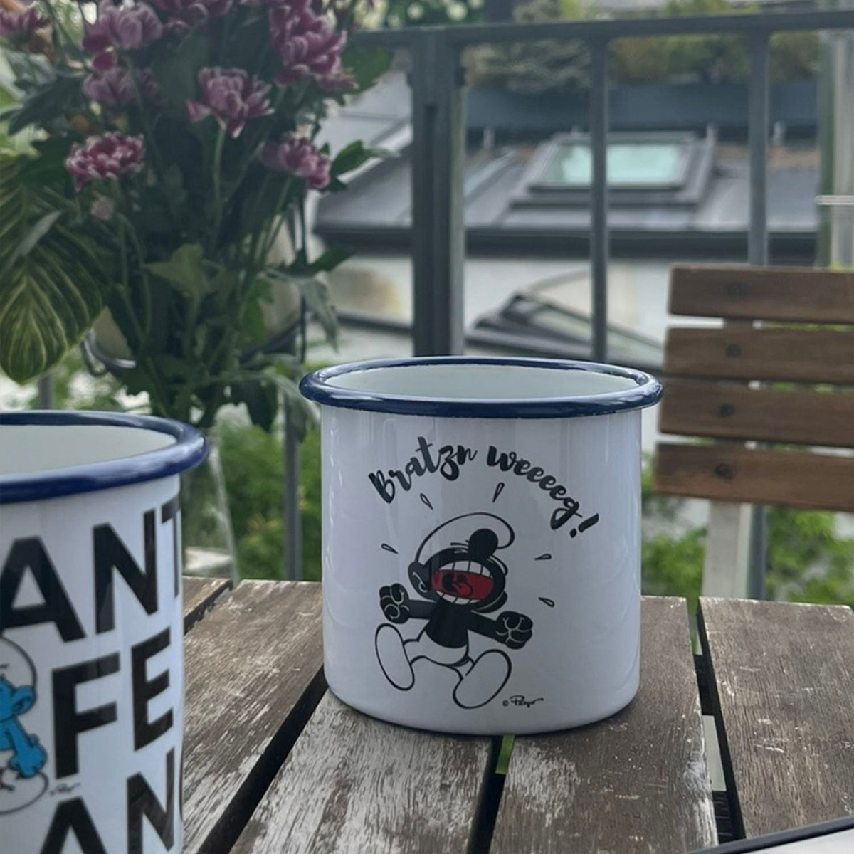 ®Die Schlümpfe Emailletasse Bratzn weg! mit lachendem Schlumpf auf rustikalem Holztisch.