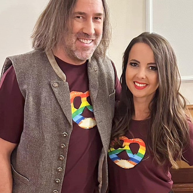 Damen T-Shirt Regenbogen-Brezn in Dunkelrot, getragen von einer lächelnden Frau, daneben ein Mann mit Weste.