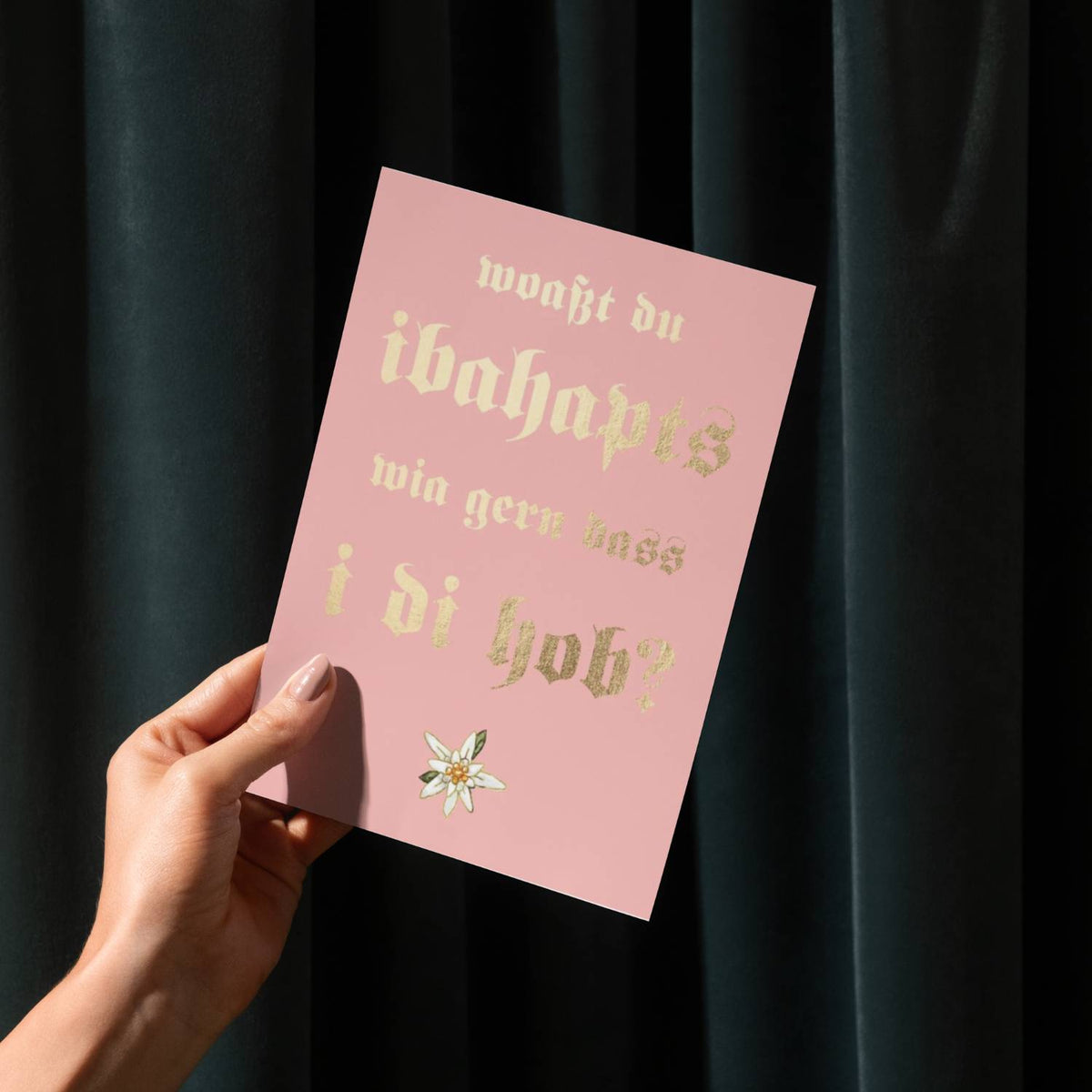 Glückwunschkarte wia gern i di hob, rosa mit goldenem Text, Edelweiß und Hand auf dunklem Hintergrund.