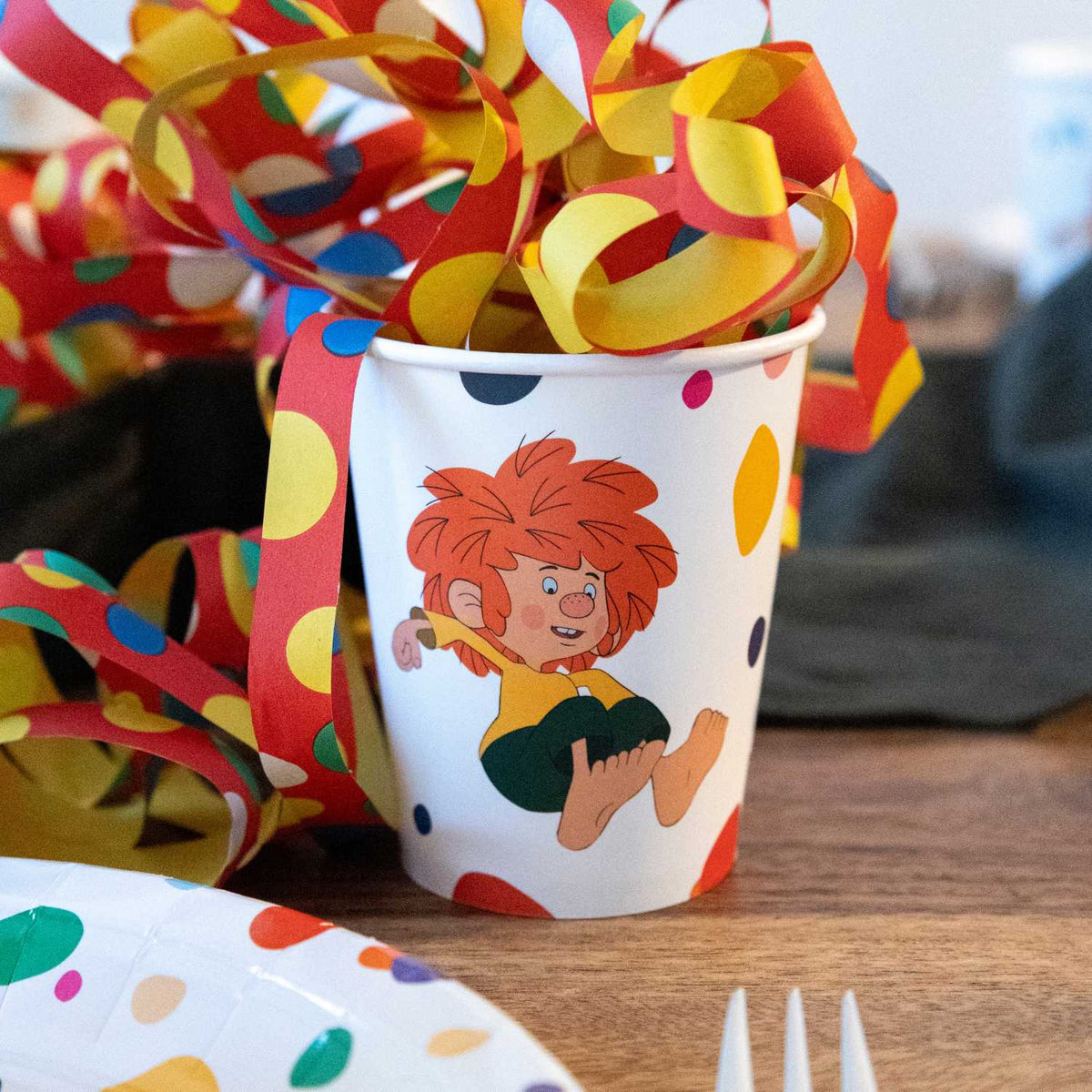 Pumuckl Pappbecher mit fröhlichem Pumuckl-Motiv zwischen bunten Luftschlangen auf der Geburtstagsfeier
