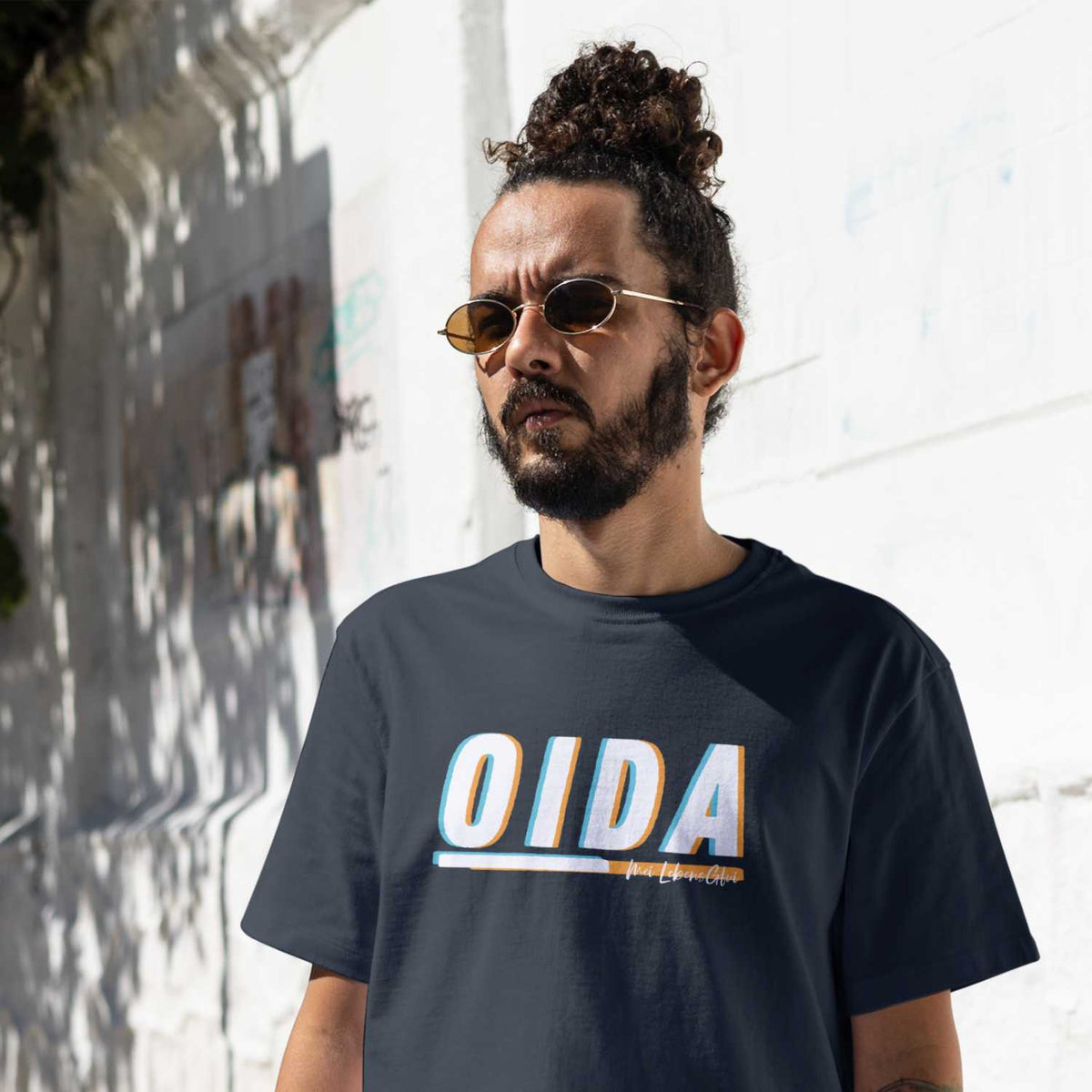 Mann mit Dutt und Sonnenbrille trägt marineblaues Herren T-Shirt Oida mit weiß-orangefarbenem Reliefdruck.