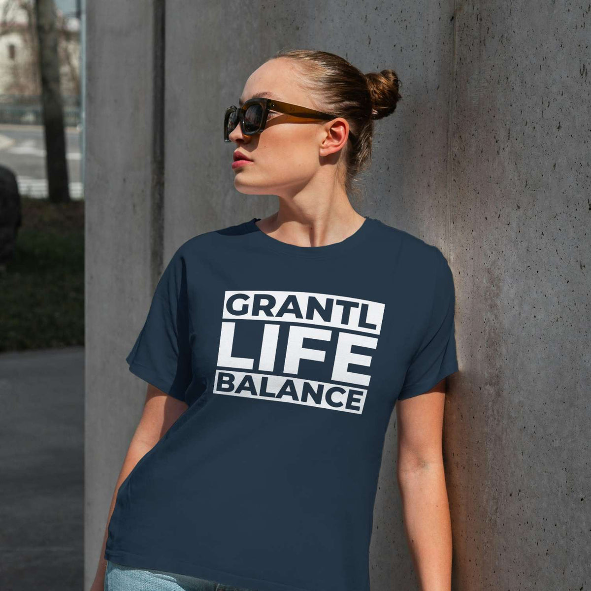 Frau in marineblauem Damen T-Shirt "Grantl Life Balance" mit weißem Schriftzug, am Pfeiler lehnend.