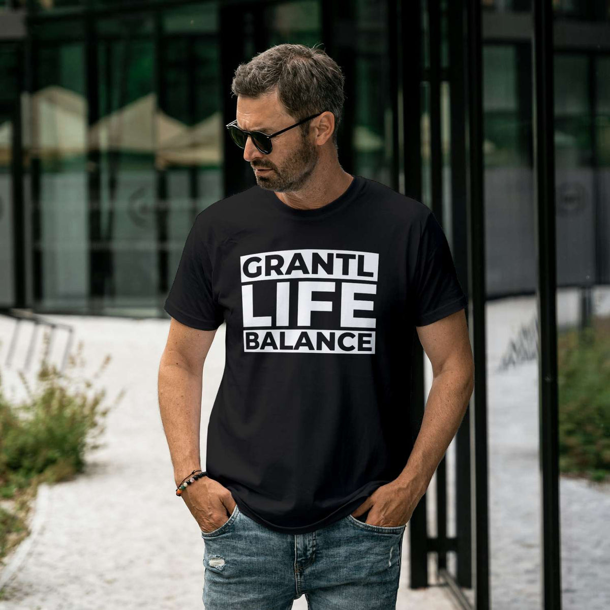 Mann trägt das schwarze Herren T-Shirt Grantl Life Balance mit weißem Schriftzug und zerrissener Jeans.