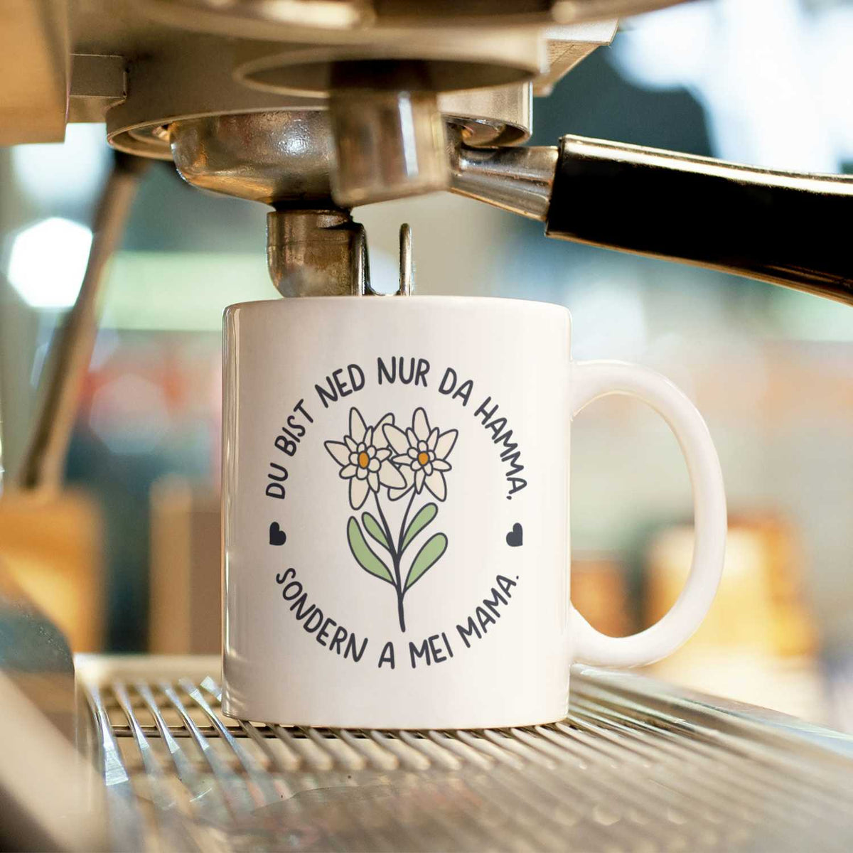 Weißes Kaffee Haferl Hamma Mama aus Keramik mit Edelweiß-Druck und bayerischem Spruch an der Kaffeemaschine.