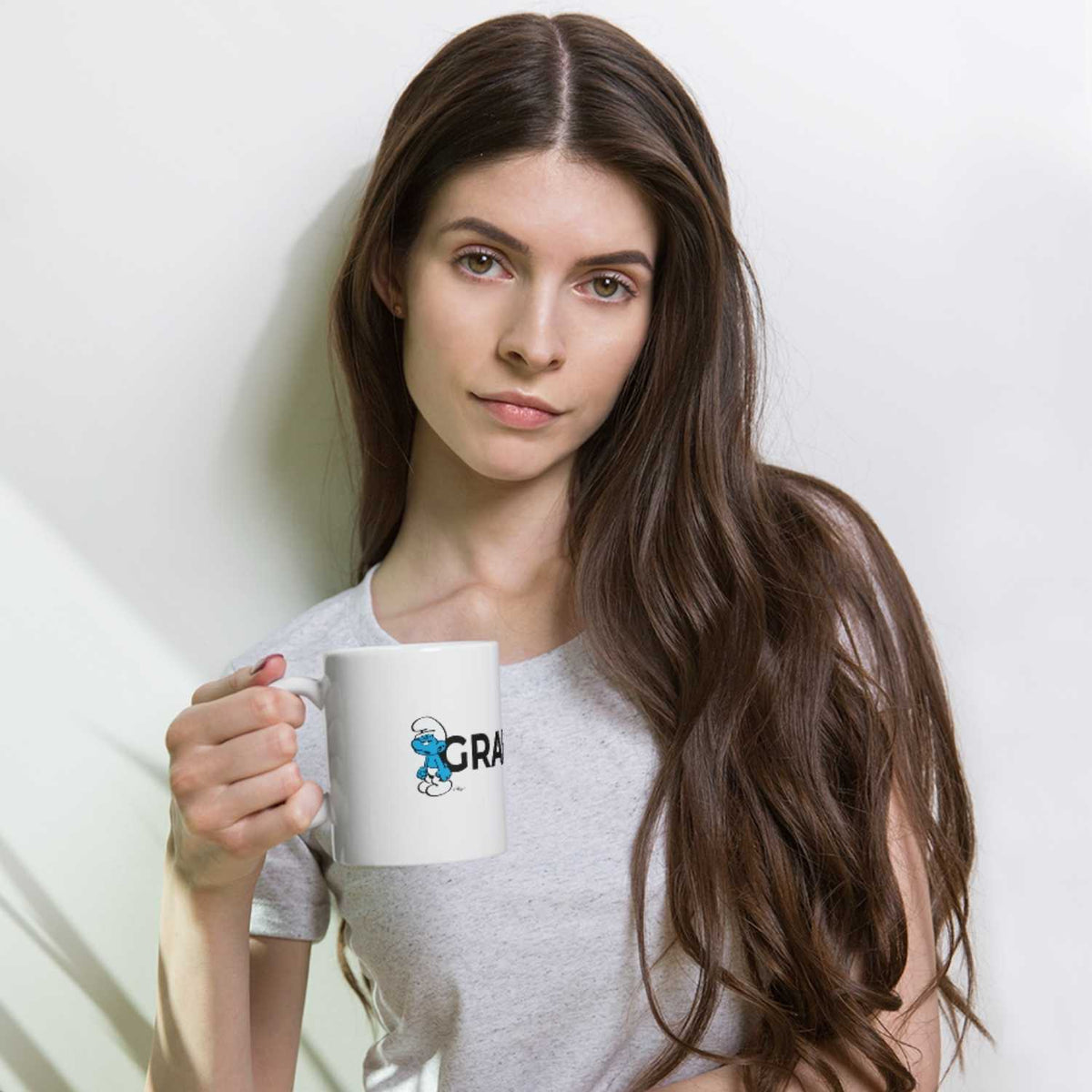 Junges Model hält weiße Schlümpfe Tasse Grantla mit brummigem Schlumpf-Motiv und schwarz-weißem Text.