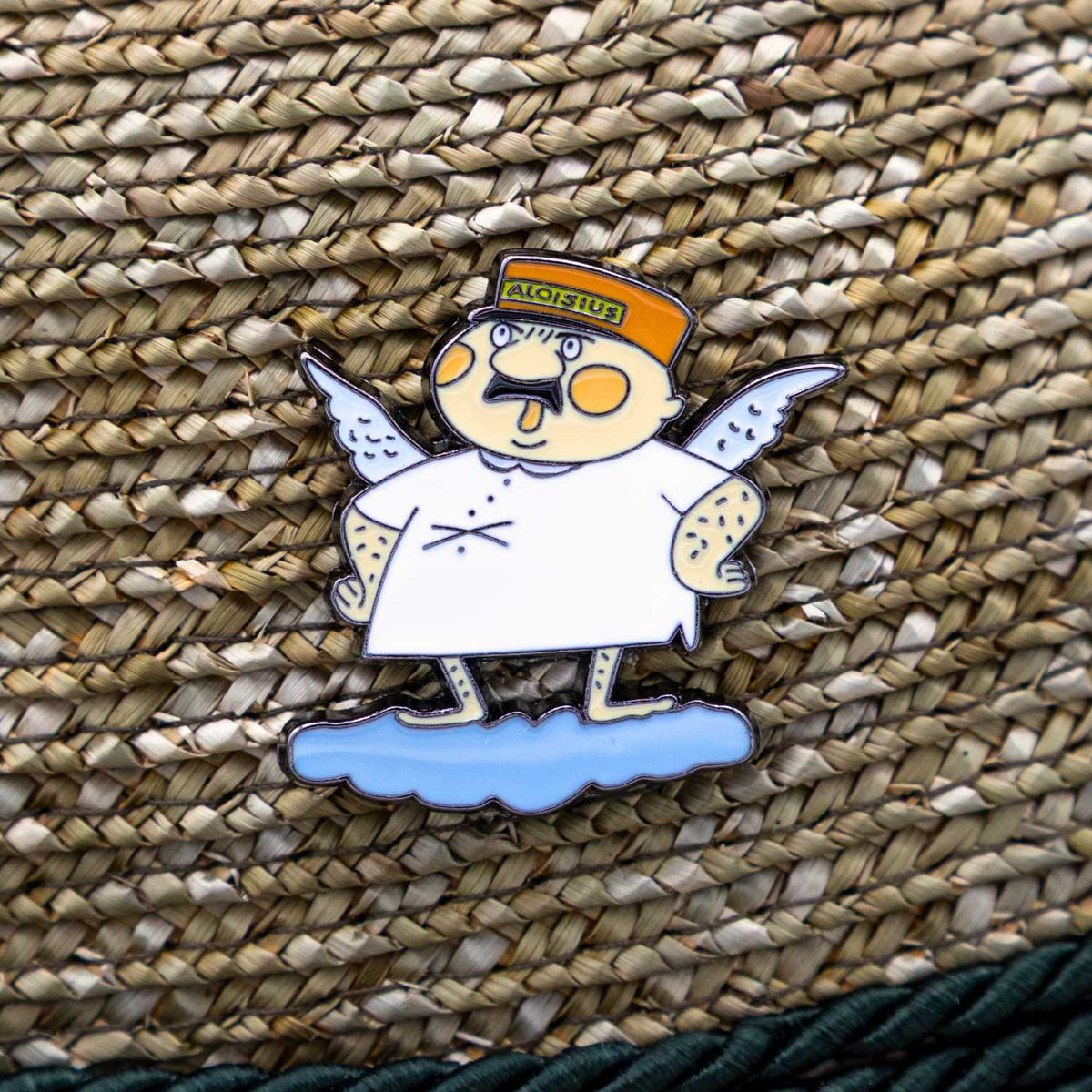 Detailaufnahme des Emaille-Pins Engel Aloisius "Luhja" auf geflochtenem Bast, humorvoller Bayern-Fanartikel.