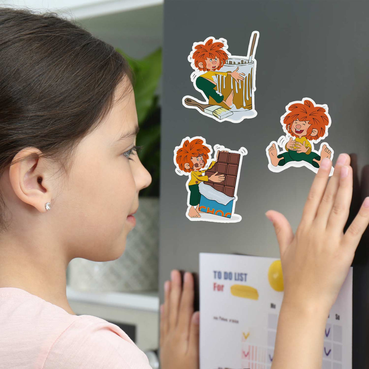 Mädchen betrachtet ®Pumuckl Sticker Set mit verschiedenen lustigen Motiven des Kobolds auf einem Kühlschrank.