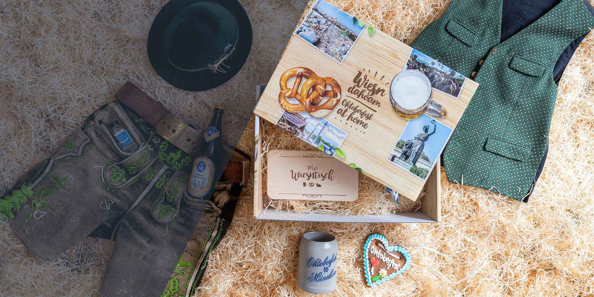 Oktoberfest Geschenkbox mit Lebkuchenherz, Trachtenweste, Lederhose, Janker und Porzellankrug auf Holzwolle.