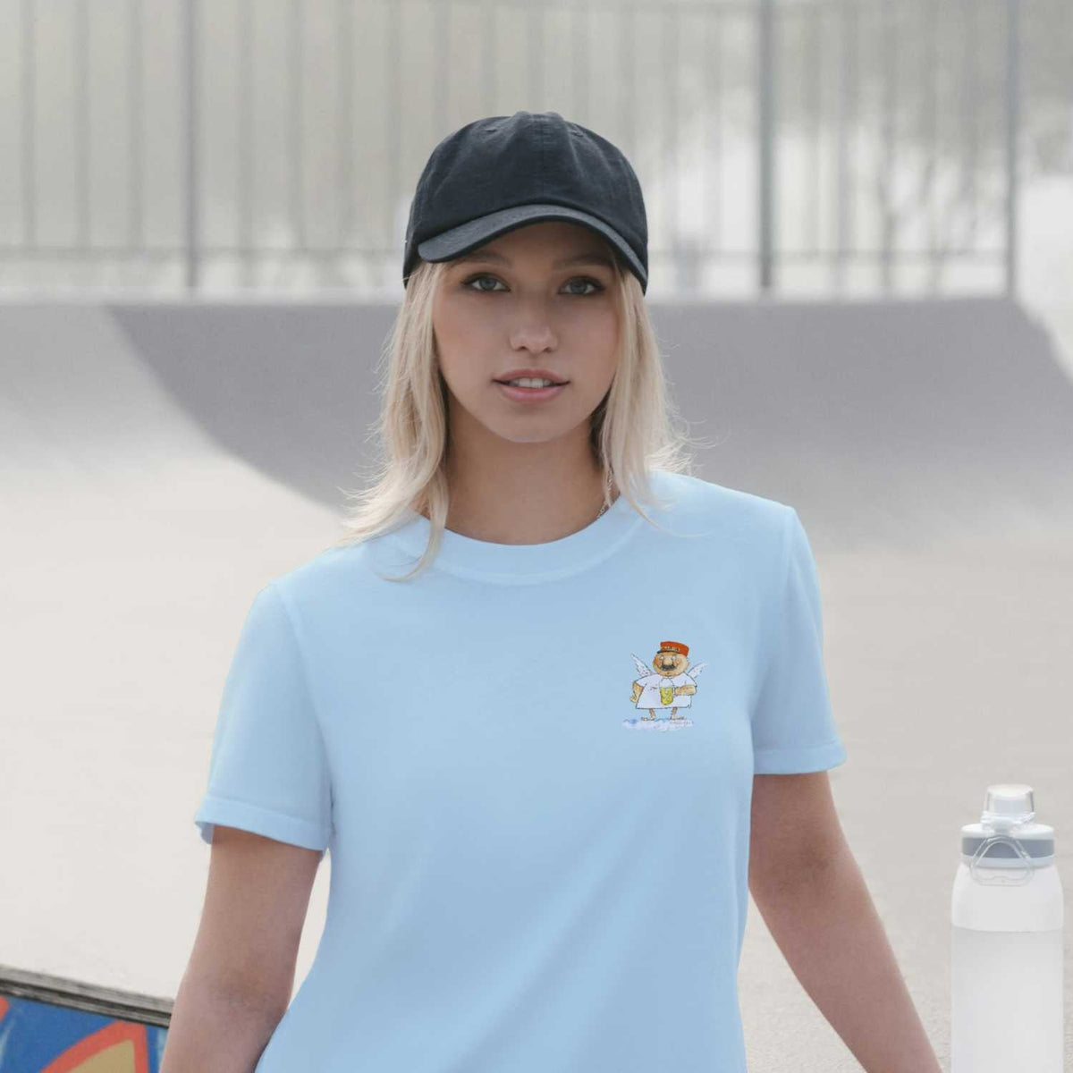 Blonde Frau trägt hellblaues Engel Aloisius Damen T-Shirt A Bier sag i mit Engel-Print, schwarzer Kappe.