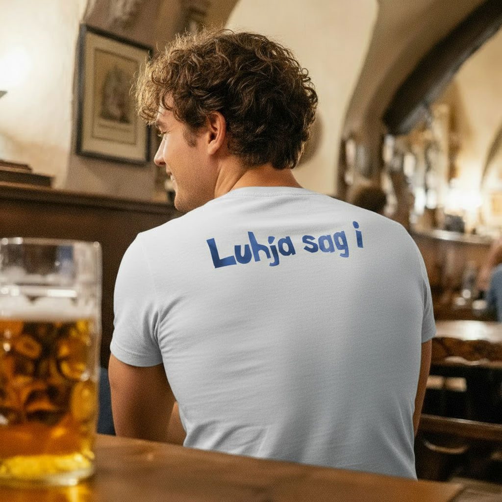 Rückenansicht eines Mannes mit lockigem Haar, der ein weißes Engel Aloisius Herren T-Shirt A Bier sag i trägt, am Tresen einer Bar sitzt.