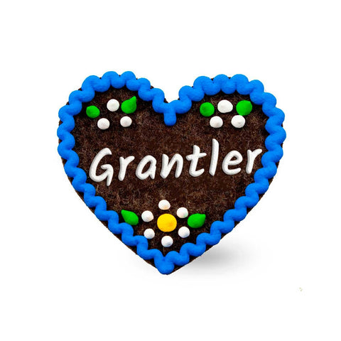 Brauner Filzherz-Anstecker "Grantler" mit blauem Zackenrand und weißen, grünen sowie gelben Verzierungen.