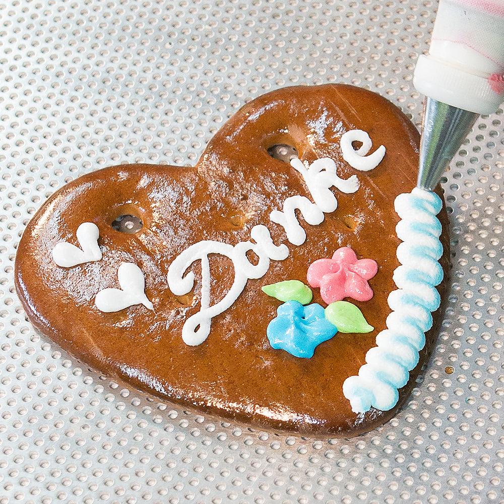 Lebkuchenherz mit weißer Zuckerschrift "Danke", bunten Blumenornamenten und blauer Bordüre, handverziert.