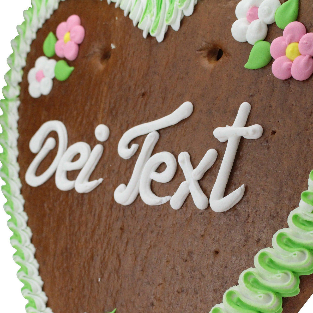 Herzförmiges Lebkuchenherz mit weißer Zuckerguss-Schrift "Dei Text", grüner Randverzierung und rosa Blumen.