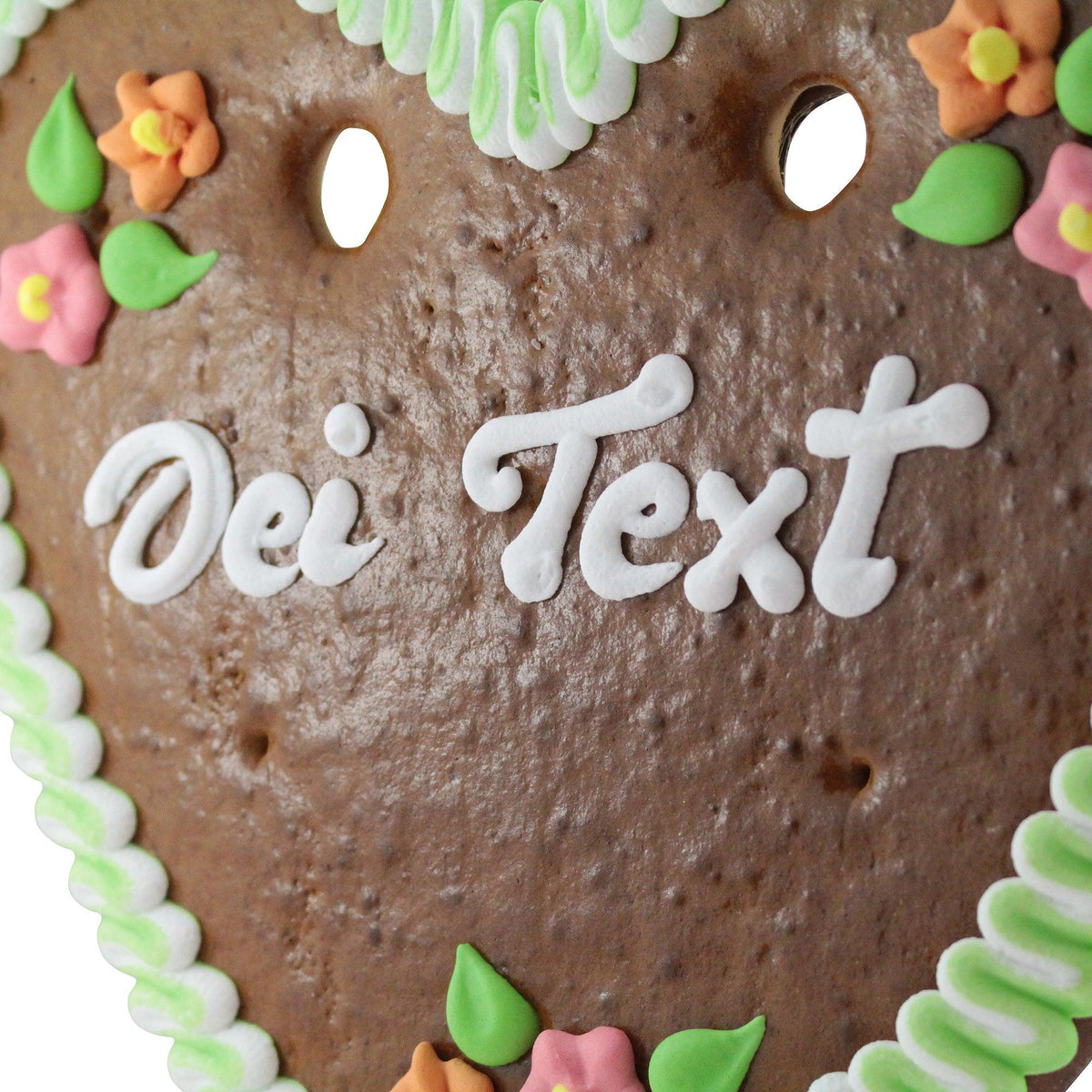 Braunes Lebkuchenherz mit weißer Zuckergussinschrift "Dei Text", verziert mit bunten Blumen und grünen Blättern.