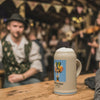 Offizieller Oktoberfestkrug 2025 mit Bier und Schaumkrone auf rustikaler Holztheke in einem Festzelt.