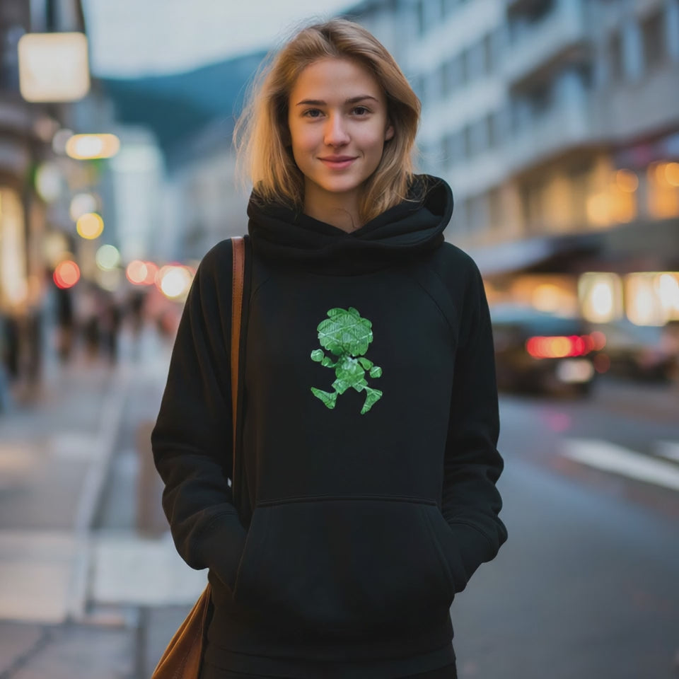Junge Frau im schwarzen Hoodie mit grünem Pumuckl-Motiv, lässig auf einer belebten Straße posierend für E-Commerce.