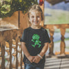 Lachendes Kind im schwarzen Pumuckl T-Shirt mit grünem Blattmuster, stehend auf einer Holzveranda