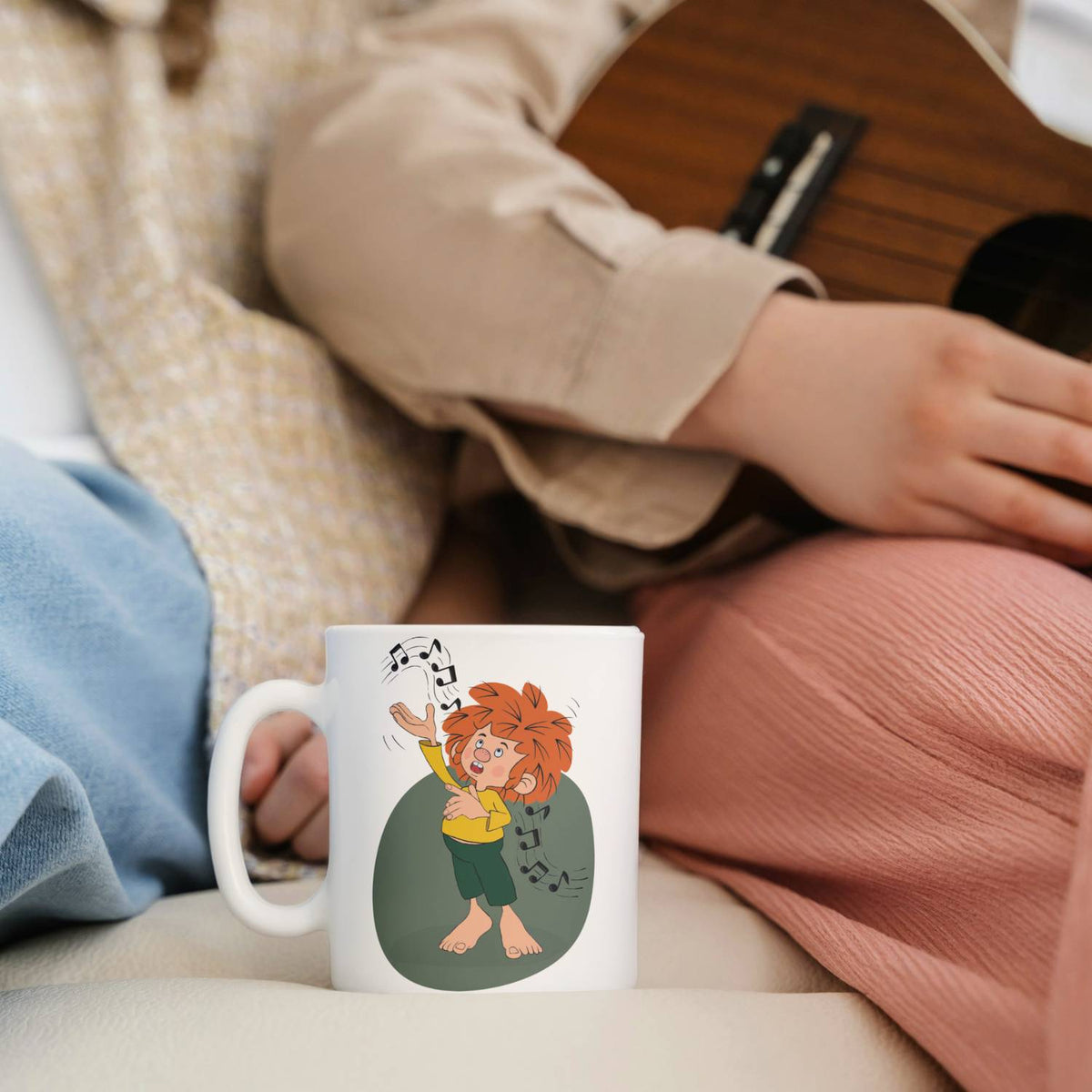 Pumuckl Tasse „Musik“ neben einer Person mit Ukulele