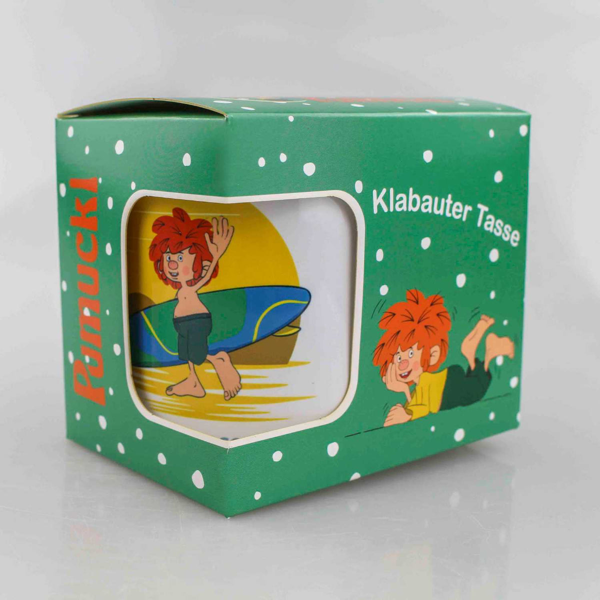 Pumuckl Tasse mit Surfer-Motiv auf grünem Geschenkkarton, Klabauter Figur mit Surfbrett am Strand.