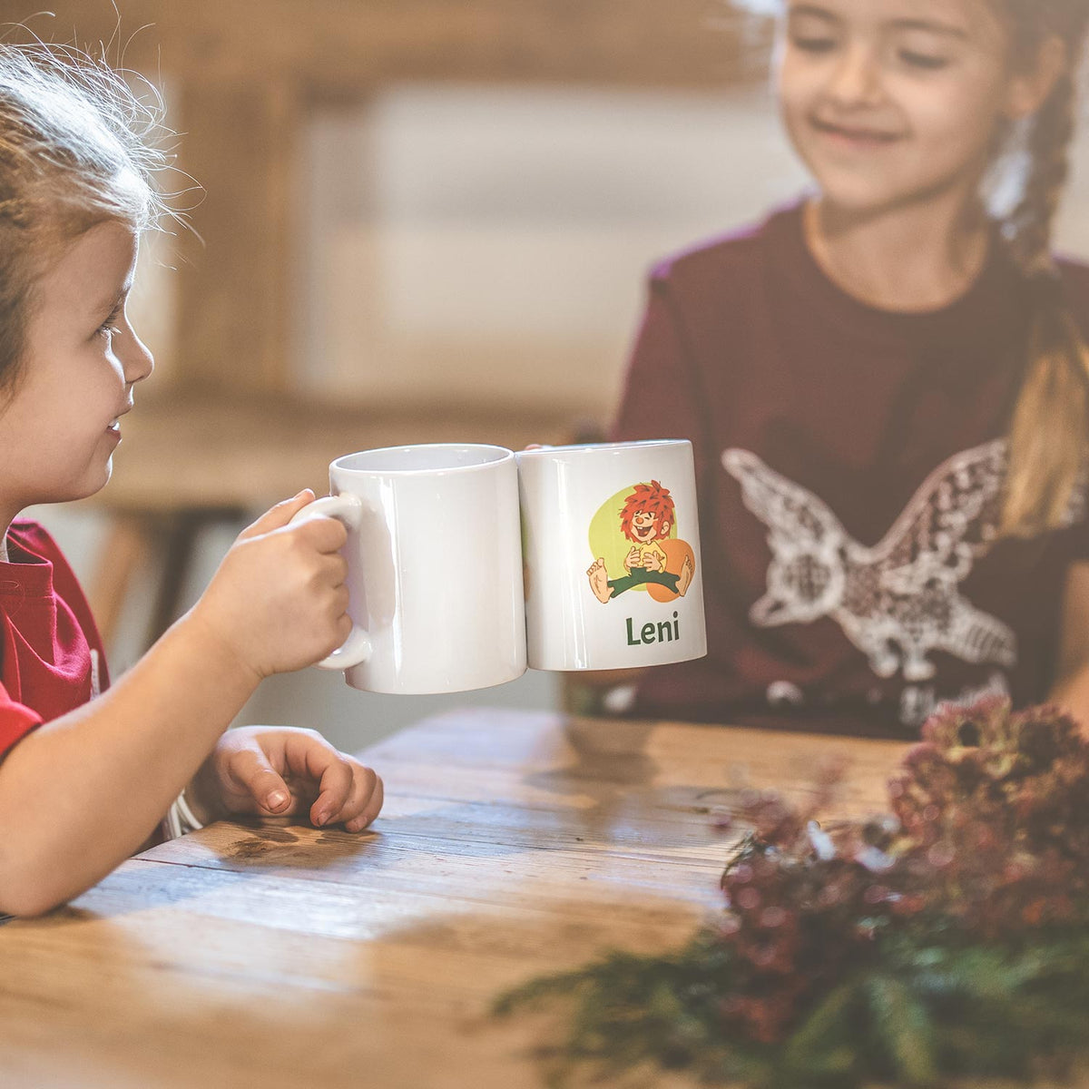 Zwei Kinder stoßen mit individuellen Tassen an: eine weiße Tasse und eine mit personalisiertem Leni-Motiv.